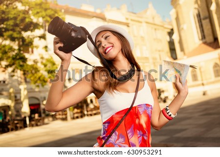 Beautiful young girl tourist holding map and photographing with digital camera.