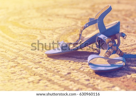 blue female sandals standing alone on antique mosaic at sunlight
