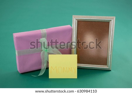 Close-up of gift box, photo frame with text mom on card against green background