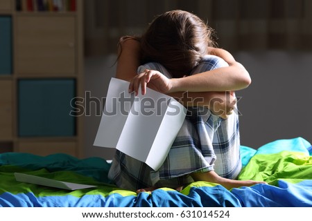 Front view of a single sad teen lamenting sitting on her bed after reading a letter with a dark light in the background Royalty-Free Stock Photo #631014524
