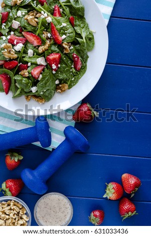 Fresh organic strawberry spinach salad with walnuts, feta cheese and poppy seed dressing on dark blue background with blue weights and salad ingredients and space for text