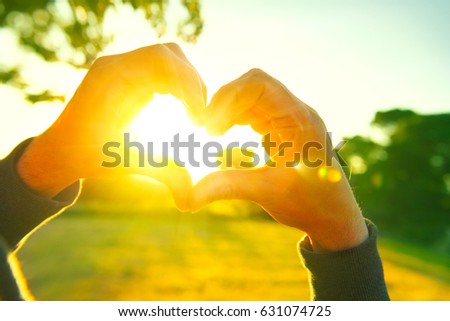 Person making heart with hands over nature sunset background. Happy young people. Silhouette hand in heart shape with sun inside. Vacation, environment concept. Summer holidays