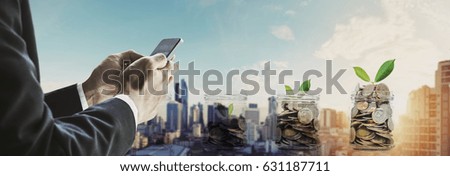 Businessman using smartphone with coins in bottles, and sunrise in the city background