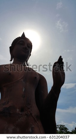 Peaceful Buddha stands and rises the left hand up to make a wish for Buddhist with the sun and little cloud in sky background at Historical park of the Sukhothai city, Thailand