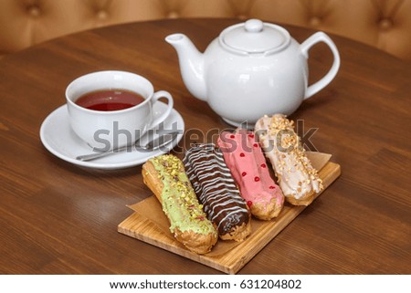 Tea and four colorful eclair cakes with cream on wooden board