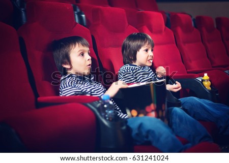 Two preschool children, twin brothers, watching movie in the cinema, eating popcorn