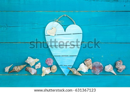 Blank broken heart sign with seashell border hanging on antique rustic teal blue background; beach sign with copy space