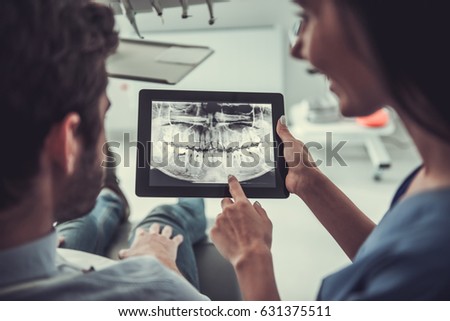 Handsome young patient and beautiful female dentist are looking at teeth image on a digital tablet