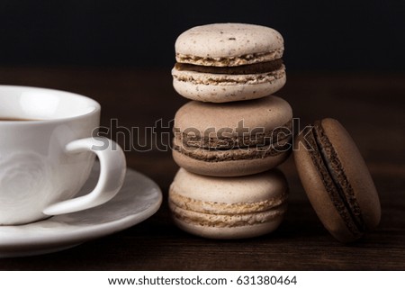 Set of coffee macaroons with a cup of coffee on dark wooden background. Cream macaroons