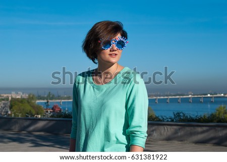 Portrait of a charming smiling girl in a funny sunglasses with flying hair during a walk in a park on a wonderful sunny morning. Modern girl during a rest in a city.