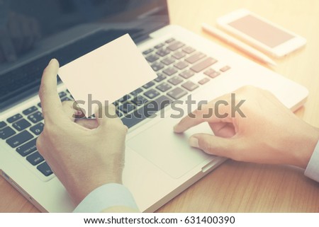 Close up female hand holding white blank business card and using laptop computer at office.
