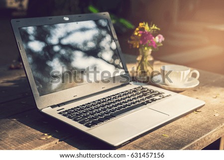 Laptop with cup of coffee on wooden table in the garden, Vintage tone