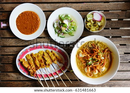 Khao soi and pork satay on wooden table. Khao soi is a northern food of Thailand Royalty-Free Stock Photo #631481663