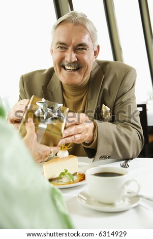 Mature Caucasian couple having dinner in nice restaurant as man gives gift to woman.