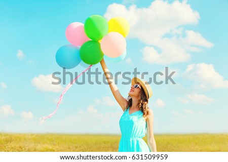 Happy smiling woman holds an air colorful balloons is enjoying a summer day on a meadow blue sky