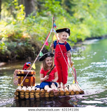 Kids dressed in pirate costumes and hats with treasure chest, spyglasses, and swords playing on wooden raft sailing in a river on hot summer day. Pirates role game for children. Water fun for family