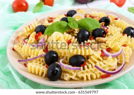 Pasta salad radiatori with chicken, black olives, blue onion, sweet pepper on a white wooden background. Close up