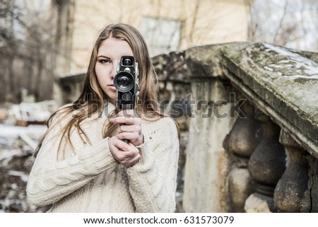 Outdoor Portrait of beautiful caucasian cute woman with brown long hair holding vintage 8mm camera in hands Outdoor in winter snowy park and based on old retro concrete fence
