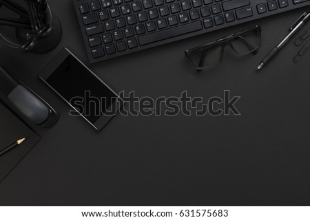 Top view of pitch black office desk with computer and supplies