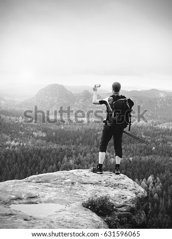 Alone tourist with outdoor sportswear and backpack stand on cliff edge  and watching into colorful autumn valley bellow.   Black and white photography