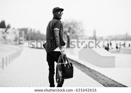 Back view portrait of walking stylish african american man wear on sunglasses and cap with handbag outdoor. Street fashion black man.