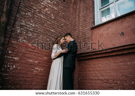 Newlyweds embracing next to red brick wall. Young wedding couple.