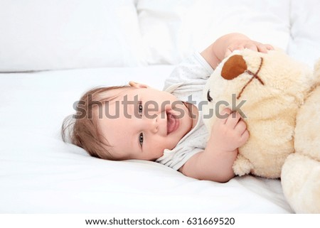 Cute baby playing with teddy bear on bed