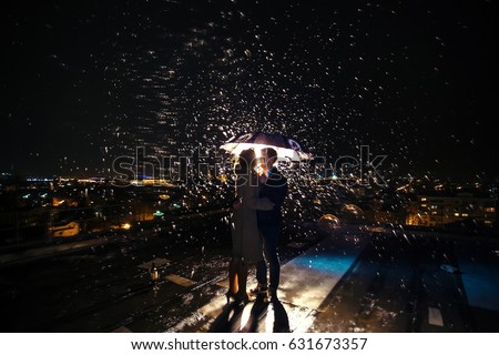 Man and woman kissing on the roof under an umbrella during the rain at night in blur