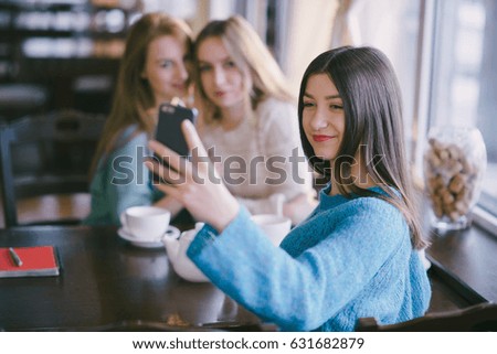 three girls sitting in a cafe at the table and use the phone