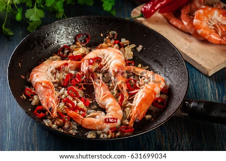 Shrimps roasted on frying pan with onion, garlic and chili on wooden background