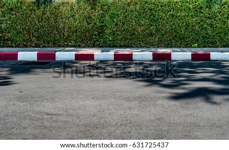 Green hedge fence with concrete road and red and white sign