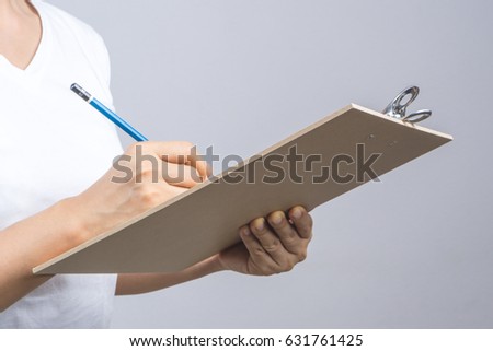 Woman hand holding wooden clipboard and a pencil on grey background Royalty-Free Stock Photo #631761425