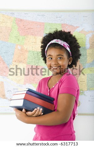African American girl standing in front of USA map holding stack of books smiling at viewer.