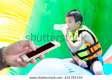 Man use mobile phone , Asian kid play and drink water inside water park as background.