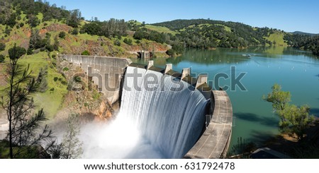 Water spills over the top of Englebright Dam on the Yuba River. A larger than normal snow pack in the Sierra Nevada Mountains has increased runoff into lakes and rivers in California. Royalty-Free Stock Photo #631792478