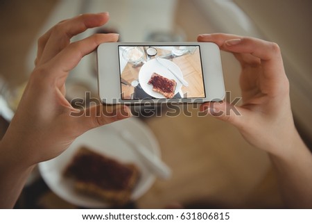 Cropped image of woman holding smart phone while photographing food at table