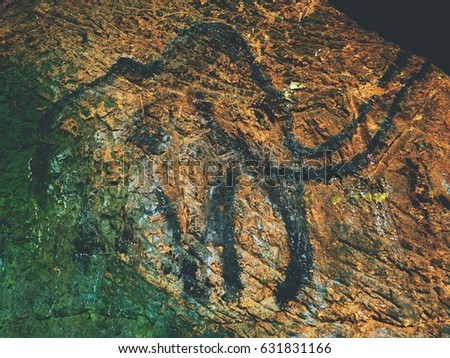  Black carbon mammoth on sandstone wall. Paint of human hunting,  prehistoric picture. Discovery of human history. Prehistoric art of mammoth in sandstone cave. Spotlight shines on historical painting
