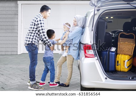 Picture of Muslim parents with their children ready to trip while standing near a car in the house garage