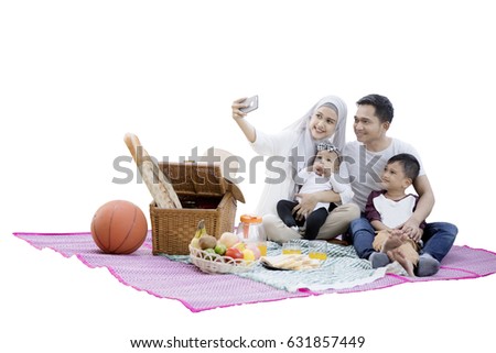 Portrait of Muslim family using a smartphone to take self pictures while enjoying a picnic in the studio