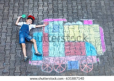 Happy little kid boy having fun with train or steam locomotive picture drawing with colorful chalks on ground. Children, lifestyle, fun concept. funny child playing and dreaming of future 