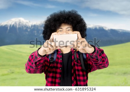 Image of afro man wearing casual clothes while using a smartphone to take a picture in the mountain