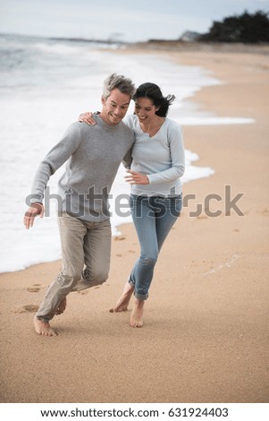 Young couple are walking on the beach, they are barefoot and wear sweaters and jeans