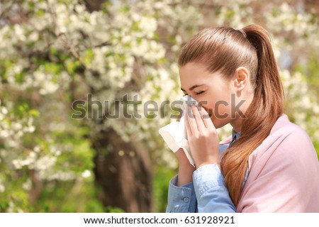 Sneezing young girl with nose wiper among blooming trees in park Royalty-Free Stock Photo #631928921