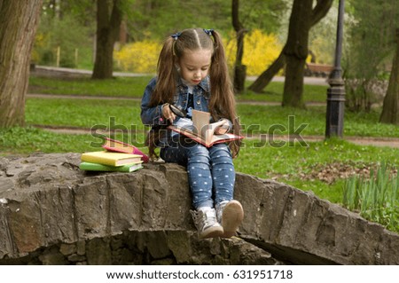 Little schoolgirl is reading a book in nature. Smart little pupil. Early development of children. Training and rest
