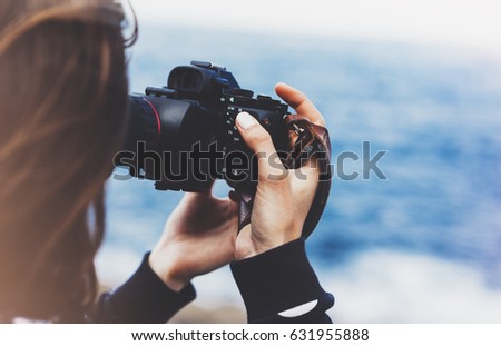 Tourist traveler photographer girl taking pictures of seascape on modern photo camera on background blue ocean view mock up sun flare, hipster female hands shoots video, nature holiday concept