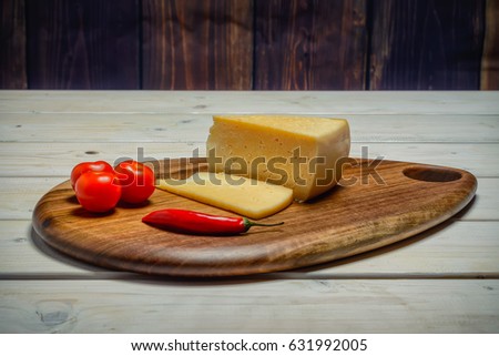 One hot pepper, three red tomatoes, cheese and sliced piece of cheese on a cutting board