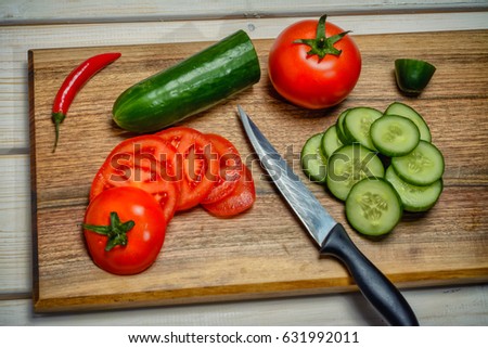 Whole tomato and pepper close cut tomato, cucumber and a kitchen knife on a cutting board