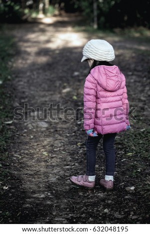 Little girl wearing a pink sweater, wearing a glove, a hat, a pair of crocheted shoes, and walking face down on the dark path to the foreground, may be fresh.