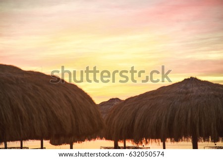Tops of old beach umbrellas made of natural materials isolated over orange sky background. Photo shot at sunrise time. Horizontal color image.