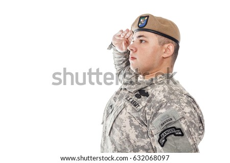 Army Ranger from Special Troops Battalion in universal Camouflage pattern Uniforms and Tan beret with Ranger Regiment crest is standing to attention and saluting proudly with honor and respect